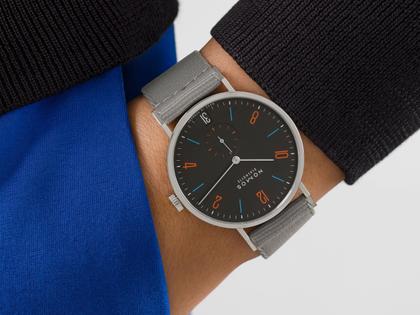 Nomos Glashütte Tangente 38 Datum "175 Years Watchmaking - Dunkelbunt" Handaufzug Edelstahl schwarzes Zifferblatt graues Textilband Glasboden – Herrenuhren Uhr mit Datum aus Edelstahl. Das Gehäuse ist rund und silber. Das Textilarmband ist grau. Das Zifferblatt ist arabisch Index und schwarz. – Ansicht 7