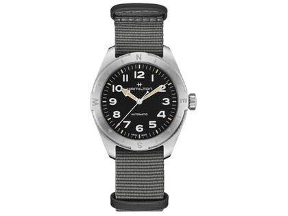 Herrenuhren Uhr ohne Datum aus Edelstahl. Das Gehäuse ist rund und silber. Das Textilarmband ist grau. Das Zifferblatt ist ein Index in schwarz.