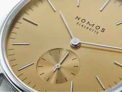 Nomos Glashütte Orion 33 Gold Handaufzug Edelstahl 33mm goldfarbenes Zifferblatt graues Lederband Glasboden – Damenuhren Uhr ohne Datum aus Edelstahl und Leder. Das Gehäuse ist rund und silber. Das Lederarmband ist beige. Das Zifferblatt ist ein Index in beige. – Ansicht 4