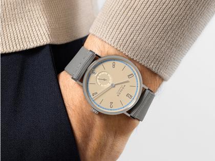 Nomos Glashütte Tangente 38 Datum "175 Years Watchmaking - Ariel" Handaufzug Edelstahl sandfarbenes Zifferblatt graues Textilband Glasboden – Herrenuhren Uhr mit Datum aus Edelstahl. Das Gehäuse ist rund und silber. Das Textilarmband ist grau. Das Zifferblatt ist arabisch Index und beige. – Ansicht 7
