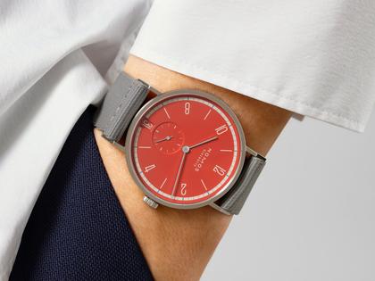 Nomos Glashütte Tangente 38 Datum "175 Years Watchmaking - Rambazamba" Handaufzug Edelstahl rotes Zifferblatt graues Textilband Glasboden – Herrenuhren Uhr mit Datum aus Edelstahl. Das Gehäuse ist rund und silber. Das Textilarmband ist grau. Das Zifferblatt ist arabisch Index und rot. – Ansicht 7