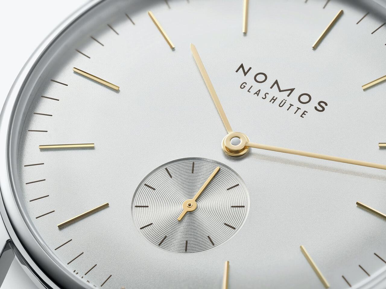 Nomos Glashütte Orion 38 Silber Handaufzug Edelstahl 38mm silberfarbenes Zifferblatt braunes Lederband Glasboden – Herrenuhren Uhr ohne Datum aus Edelstahl. Das Gehäuse ist rund und silber. Das Lederarmband ist grau. Das Zifferblatt ist ein Index in silber. – Ansicht 2