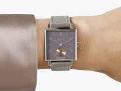 Nomos Glashütte Tetra Die Fuchsteufelswilde Handaufzug Edelstahl 29mm violettes Zifferblatt graues Veloursband Glasboden – Damenuhren Uhr ohne Datum aus Edelstahl und Leder. Das Gehäuse ist quadratisch und silber. Das Lederarmband ist grau. Das Zifferblatt ist arabisch Index und lila. – Ansicht 4