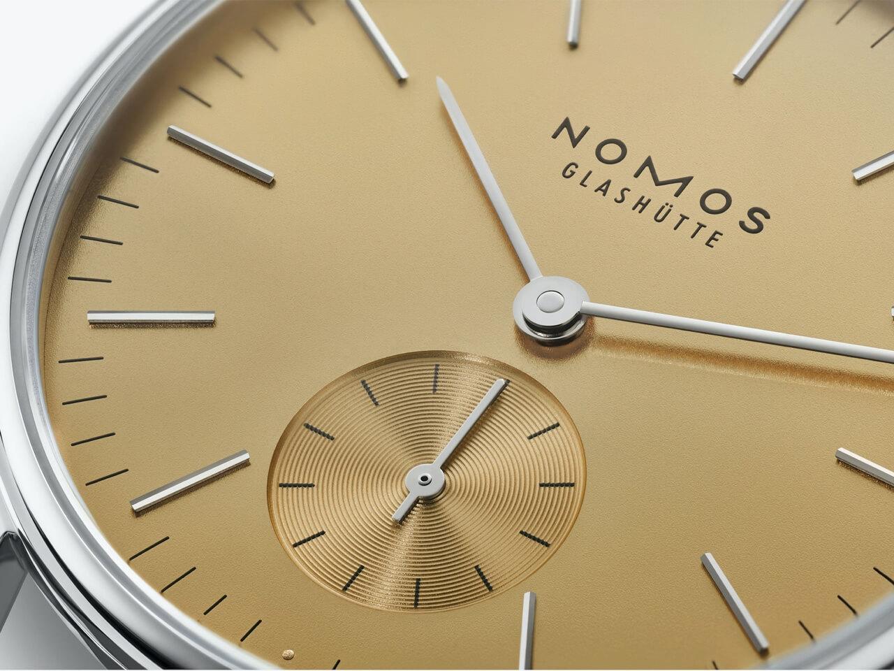 Nomos Glashütte Orion 33 Gold Handaufzug Edelstahl 33mm goldfarbenes Zifferblatt graues Lederband Glasboden – Damenuhren Uhr ohne Datum aus Edelstahl und Leder. Das Gehäuse ist rund und silber. Das Lederarmband ist beige. Das Zifferblatt ist ein Index in beige. – Ansicht 4
