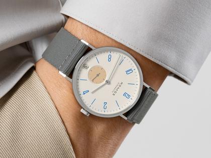 Nomos Glashütte Tangente 38 Datum "175 Years Watchmaking - Schulhausweiß" Handaufzug Edelstahl cremeweißes Zifferblatt graues Textilband Glasboden – Herrenuhren Uhr mit Datum aus Edelstahl. Das Gehäuse ist rund und silber. Das Textilarmband ist grau. Das Zifferblatt ist arabisch Index und beige. – Ansicht 7