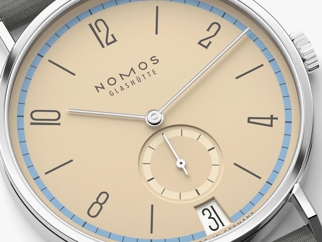 Nomos Glashütte Tangente 38 Datum "175 Years Watchmaking - Ariel" Handaufzug Edelstahl sandfarbenes Zifferblatt graues Textilband Glasboden – Herrenuhren Uhr mit Datum aus Edelstahl. Das Gehäuse ist rund und silber. Das Textilarmband ist grau. Das Zifferblatt ist arabisch Index und beige. – Ansicht 4