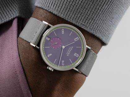 Nomos Glashütte Tangente 38 Datum "175 Years Watchmaking - Mauvegrün" Handaufzug Edelstahl violettes Zifferblatt graues Textilband Glasboden – Herrenuhren Uhr mit Datum aus Edelstahl. Das Gehäuse ist rund und silber. Das Textilarmband ist grau. Das Zifferblatt ist arabisch Index und lila. – Ansicht 7